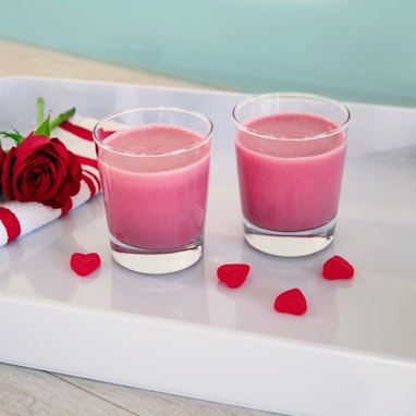 Two glasses of beet smoothie and pink nutribullet blender in front of a floral backdrop 