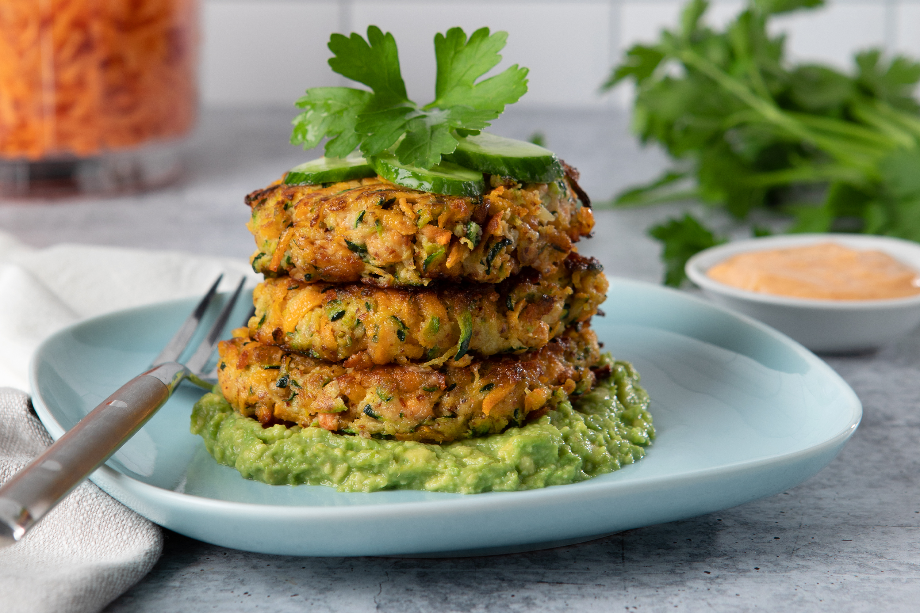 stack of zucchini fritters over guacamole and topped with cucumber and parsley