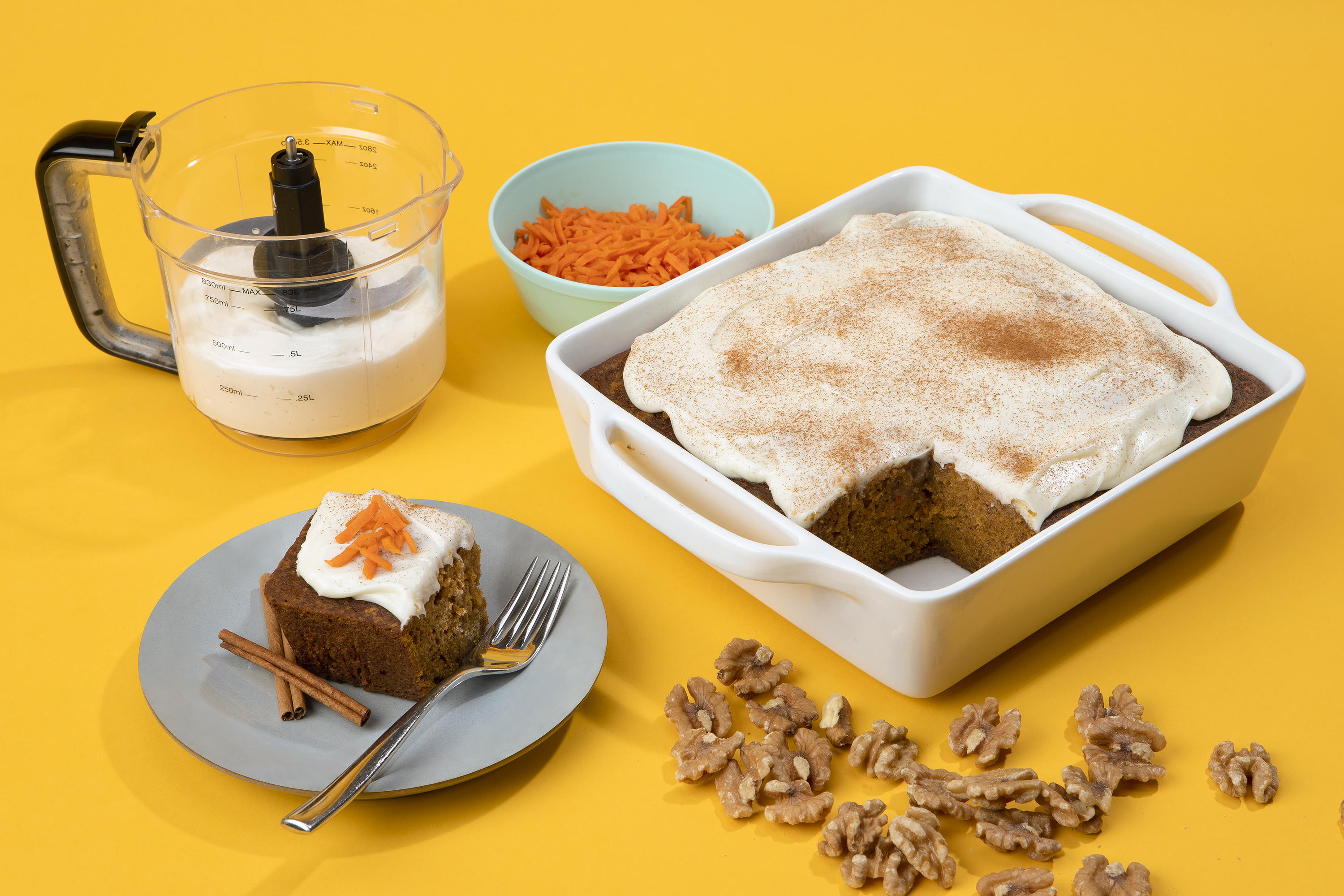 slice of carrot cake with cream cheese frosting  and walnuts on plate with more in dish