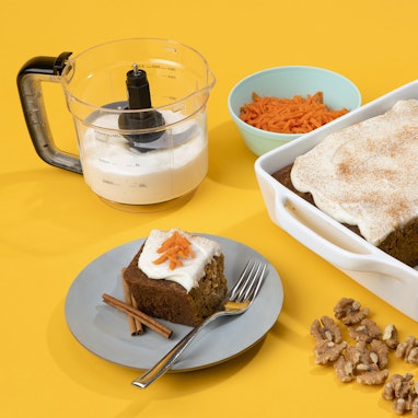slice of carrot cake with cream cheese frosting  and walnuts on plate with more in dish