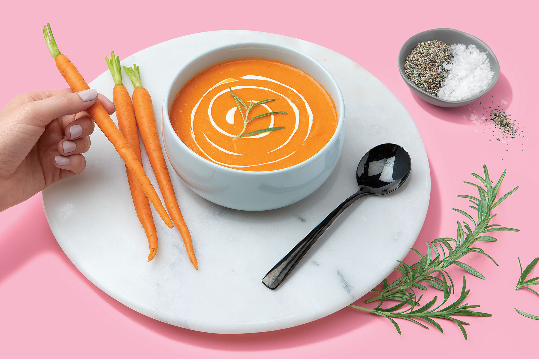 bowl of carrot soup with crema, fresh carrots, and salt and pepper