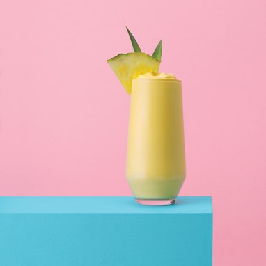 glass of blended pina colada cocktail with pineapple slice