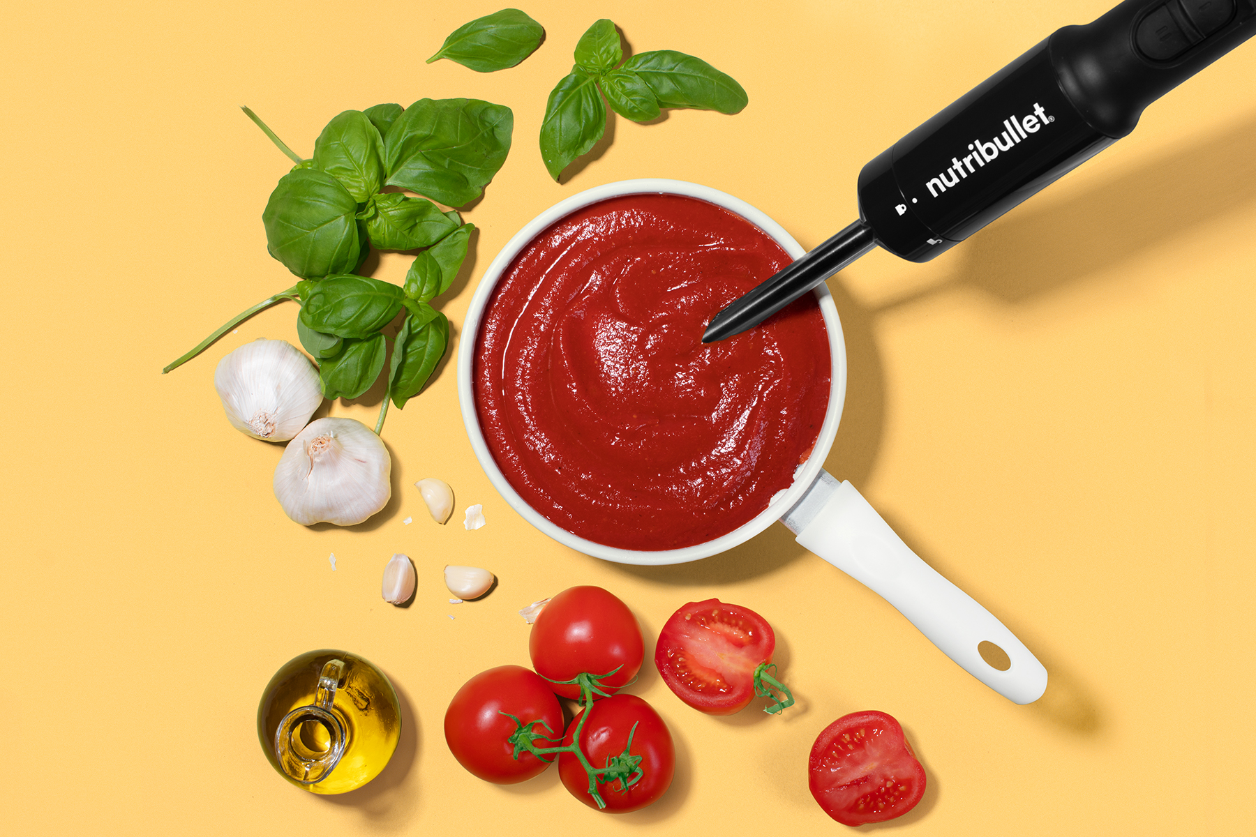 immersion blender in bowl of marinara with tomato, olive oil, garlic, and basil 