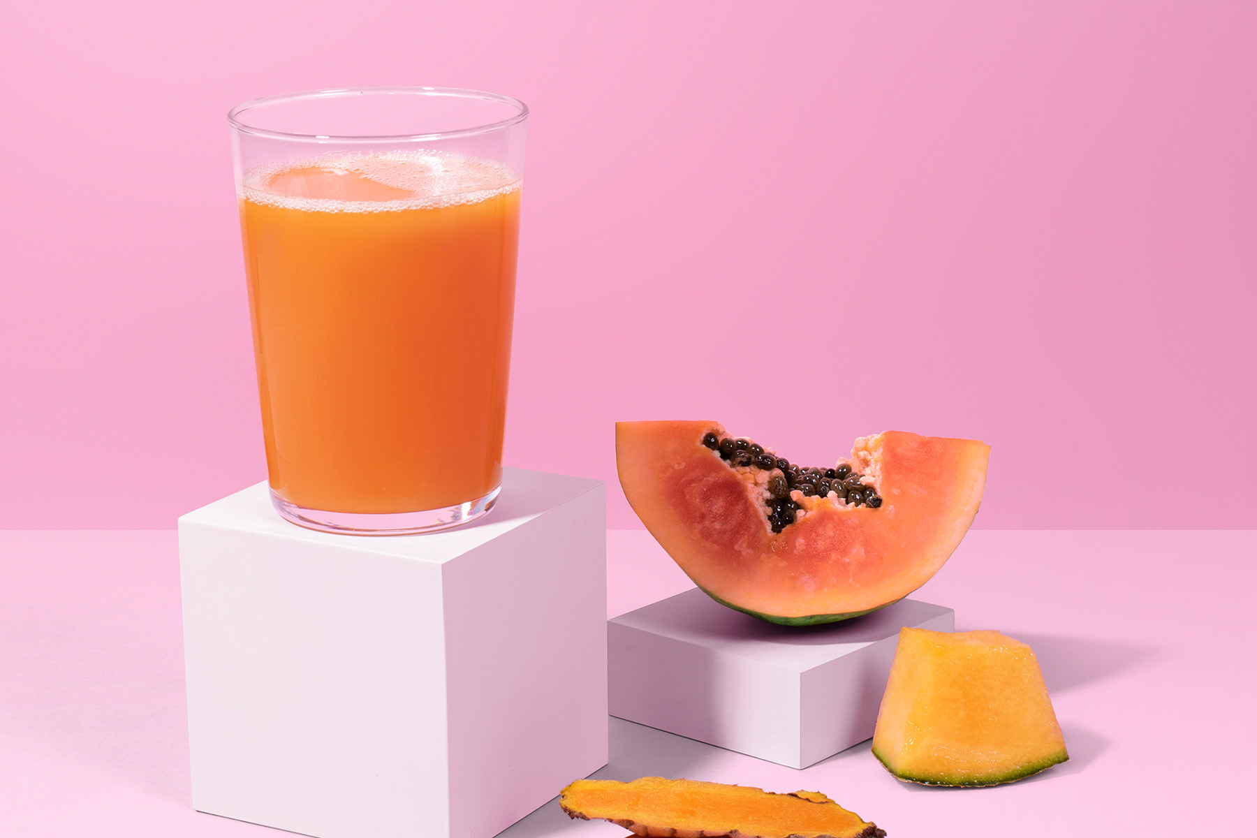 glass of papaya juice with sliced papaya, cantaloupe, and turmeric