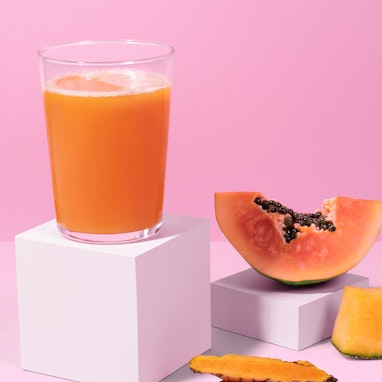 glass of papaya juice with sliced papaya, cantaloupe, and turmeric