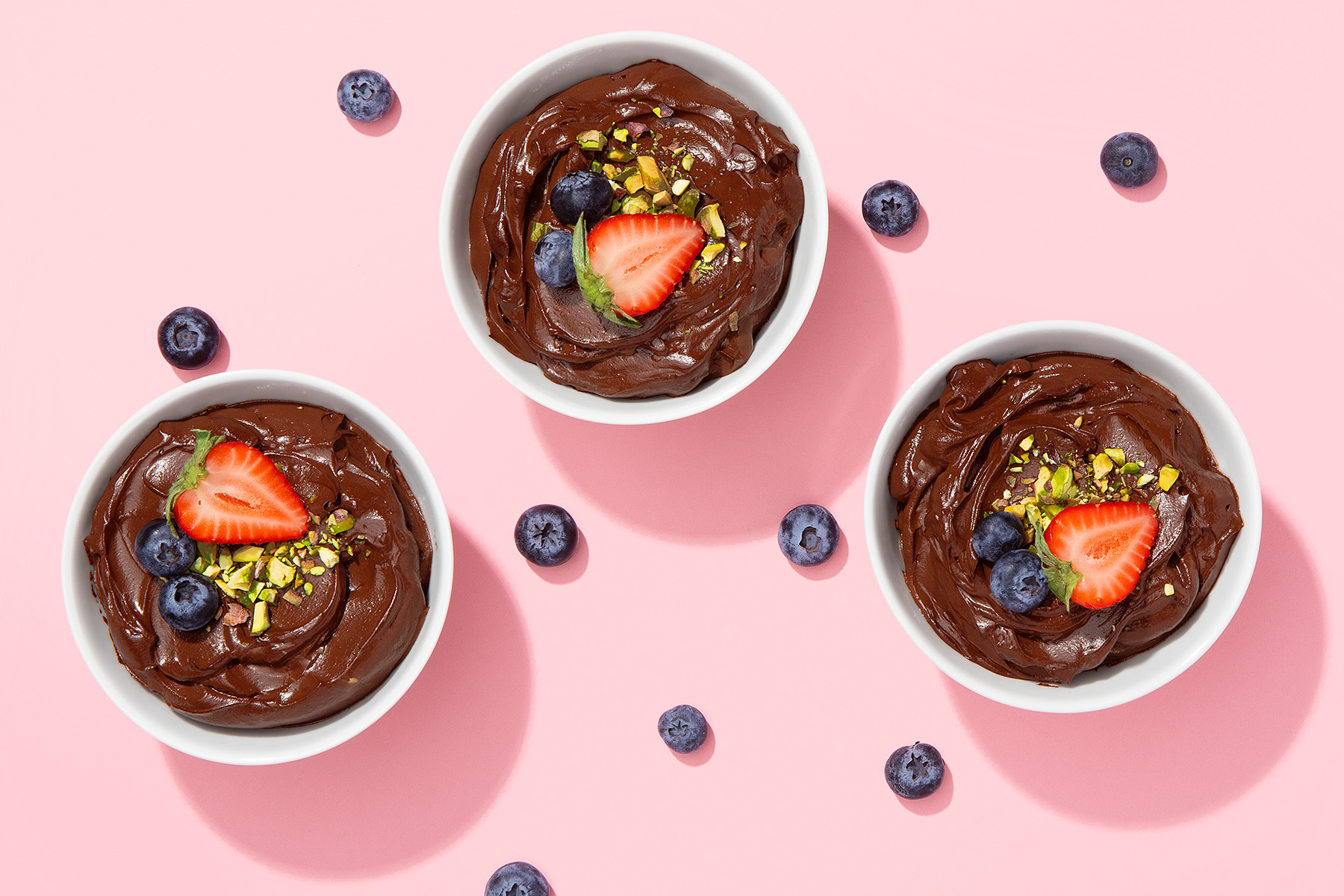 three bowls of coffee mocha avocado pudding with fresh berries and pistachio