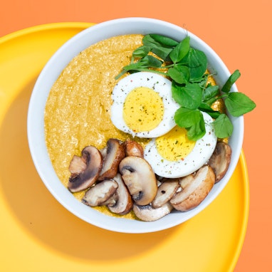 bowl of amaranth polenta with eggs, mushrooms, and pea shoots