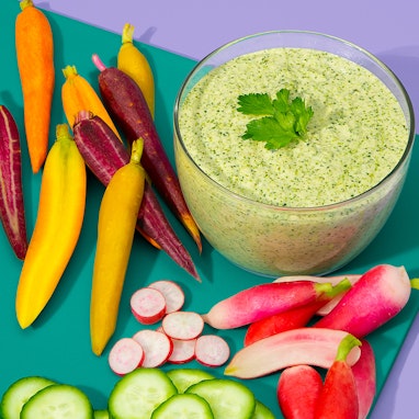 clear bowl of green goddess dressing with fresh carrots and radishes for dipping