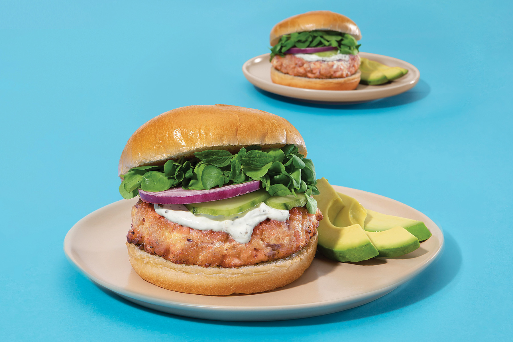 plate of salmon burger on a bun with avocado, onion, lettuce and pickles