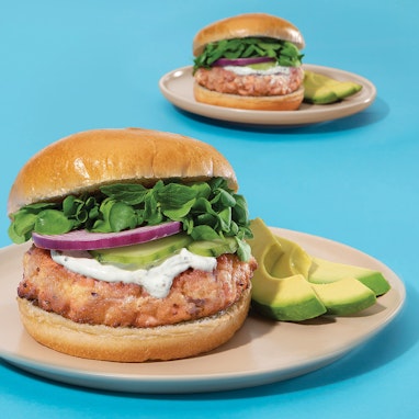 plate of salmon burger on a bun with avocado, onion, lettuce and pickles