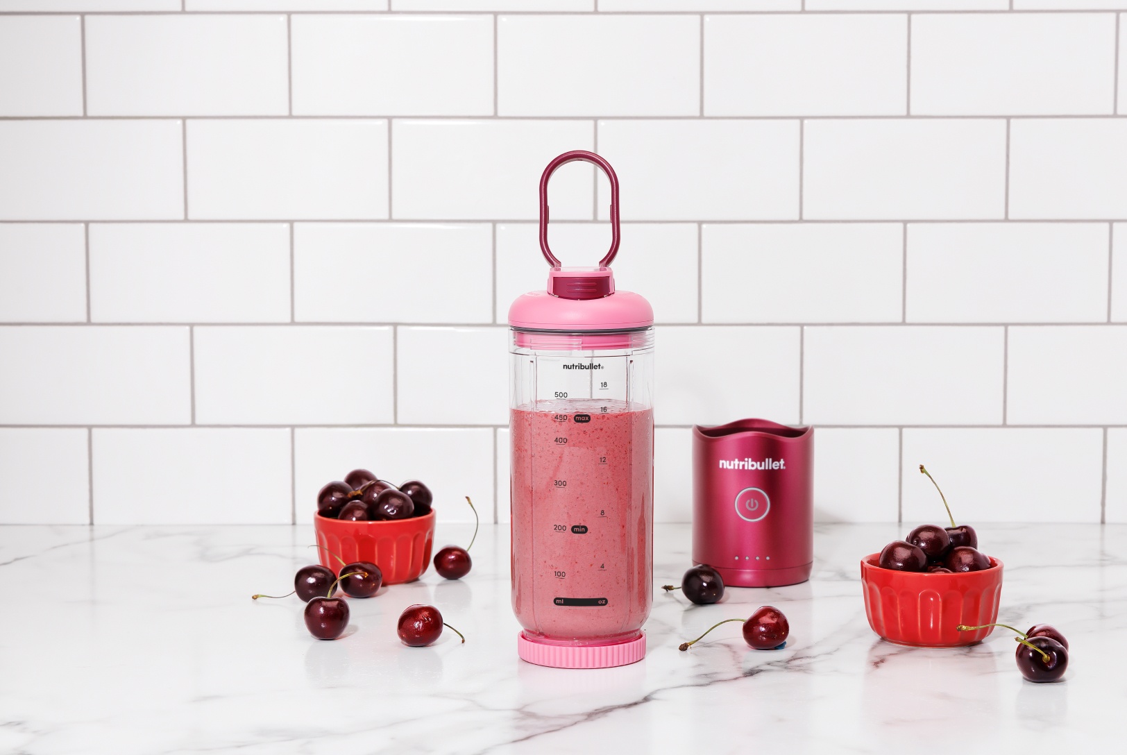 pink cherry smoothie in a portable blender, detached next to two small bowls of fresh cherries