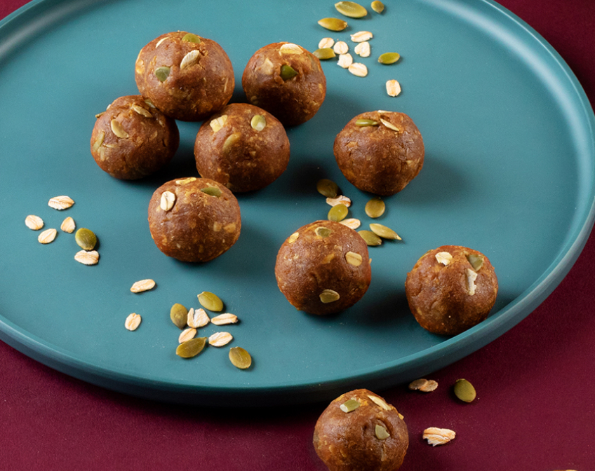 Eight protein balls on a blue plate with oats and pumpkin seeds.